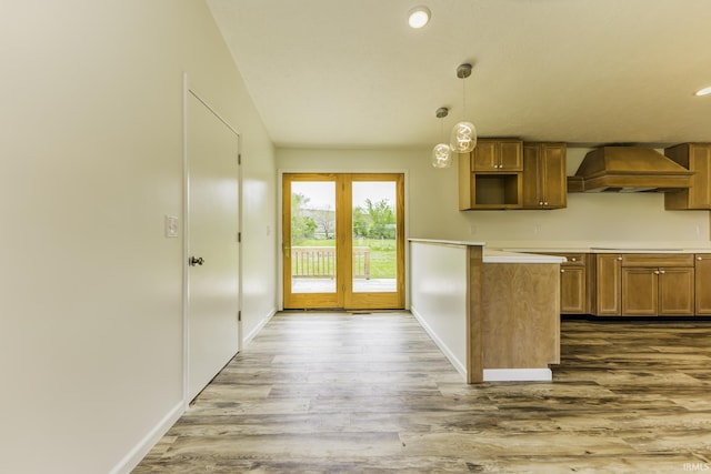 kitchen featuring brown cabinetry, decorative light fixtures, wood finished floors, baseboards, and custom exhaust hood
