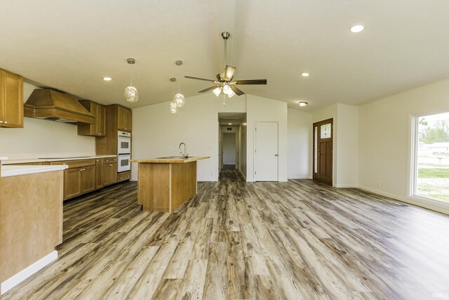kitchen featuring wood finished floors, white double oven, premium range hood, lofted ceiling, and open floor plan