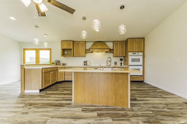 kitchen featuring double oven, baseboards, wood finished floors, and premium range hood