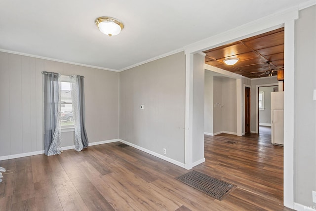spare room featuring baseboards, crown molding, wood finished floors, and visible vents