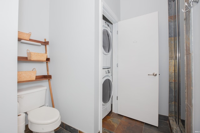 bathroom with stone tile floors, toilet, an enclosed shower, and stacked washer / dryer