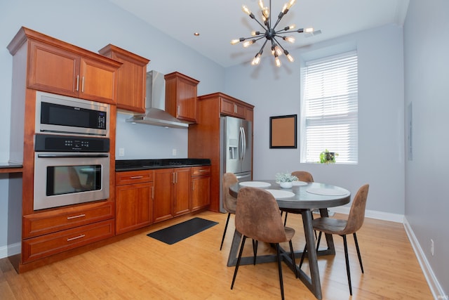 kitchen with an inviting chandelier, light wood-style flooring, wall chimney exhaust hood, and appliances with stainless steel finishes