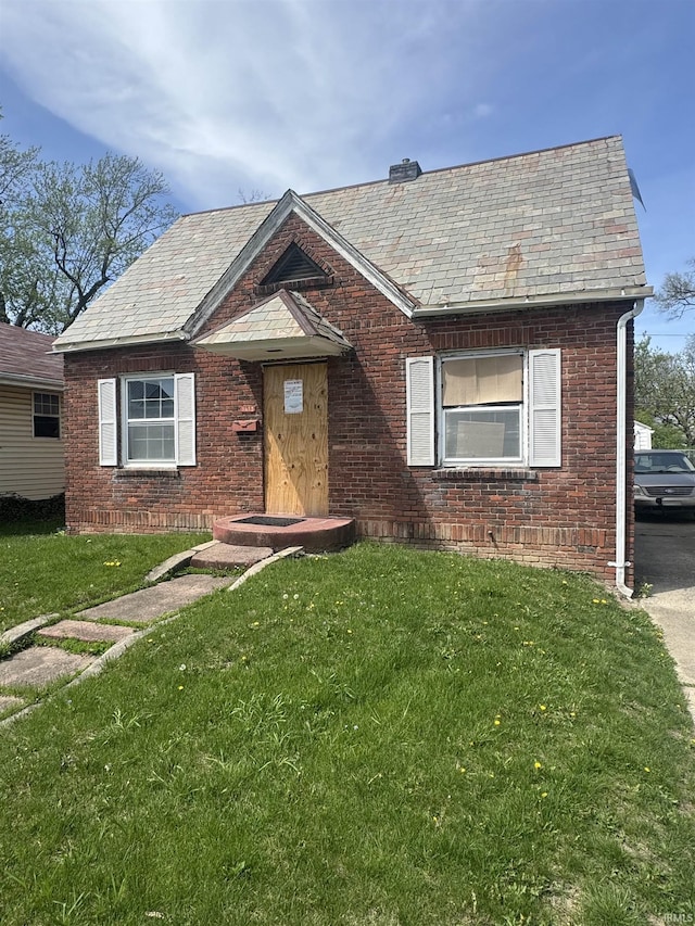 view of front facade with a front yard, a high end roof, and brick siding