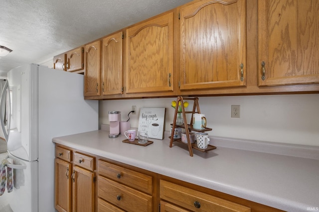 kitchen featuring light countertops, a textured ceiling, brown cabinetry, and freestanding refrigerator