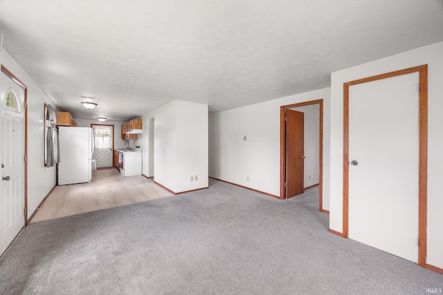unfurnished living room featuring baseboards, washing machine and dryer, and light colored carpet