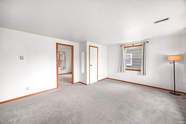 carpeted spare room featuring baseboards, visible vents, and plenty of natural light