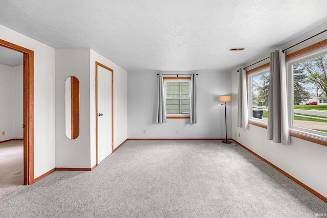 unfurnished room featuring baseboards, carpet flooring, a textured ceiling, and visible vents