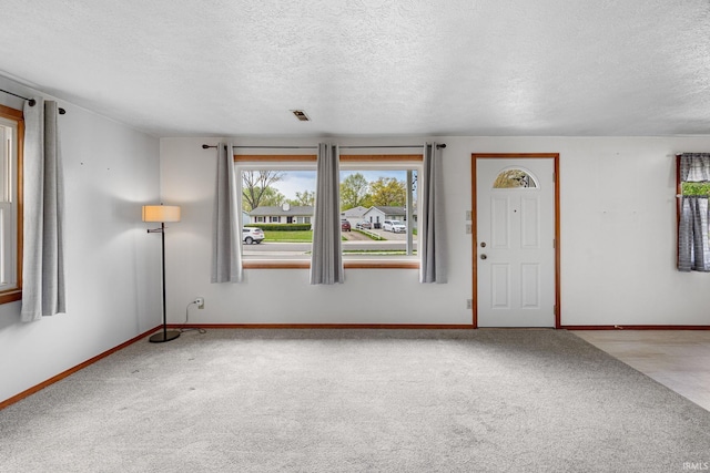 foyer with baseboards, carpet, a textured ceiling, and visible vents