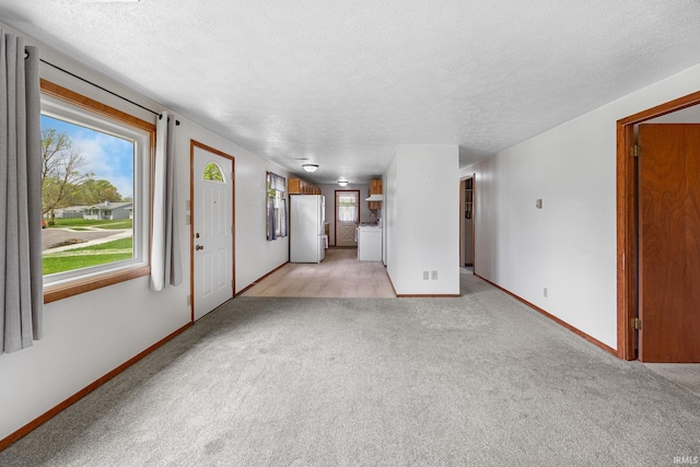 unfurnished living room with independent washer and dryer, a textured ceiling, light carpet, and baseboards