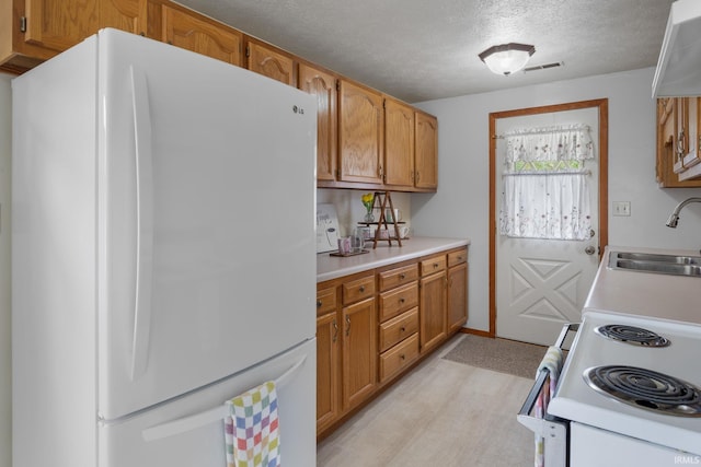 kitchen featuring a textured ceiling, visible vents, a sink, light countertops, and white appliances