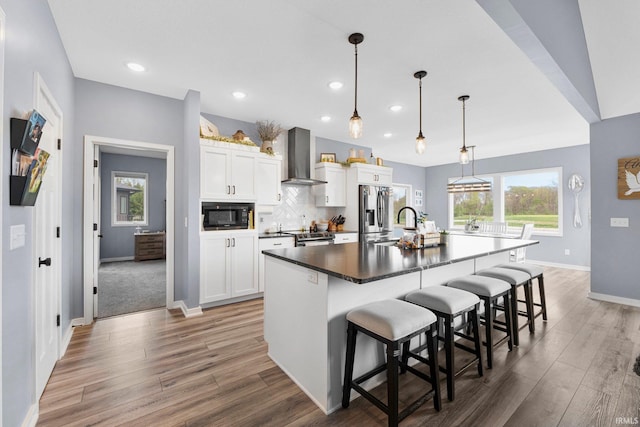 kitchen featuring appliances with stainless steel finishes, baseboards, light wood-type flooring, and wall chimney exhaust hood