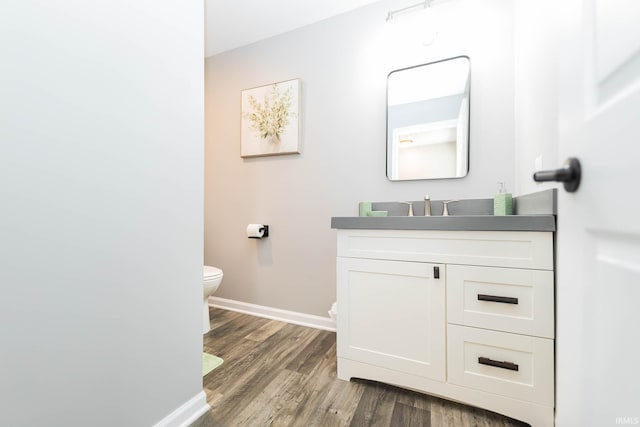 half bath featuring toilet, baseboards, wood finished floors, and vanity