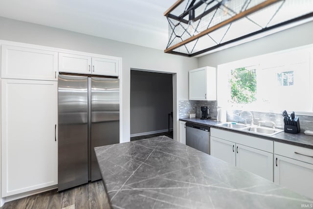 kitchen featuring white cabinetry, a sink, dark wood finished floors, appliances with stainless steel finishes, and backsplash