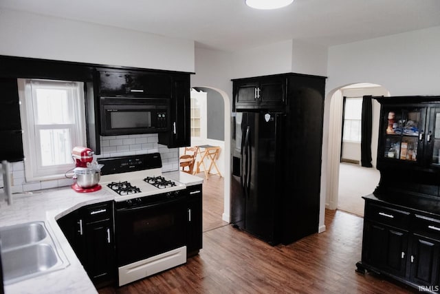 kitchen featuring dark cabinetry, arched walkways, black appliances, and light countertops