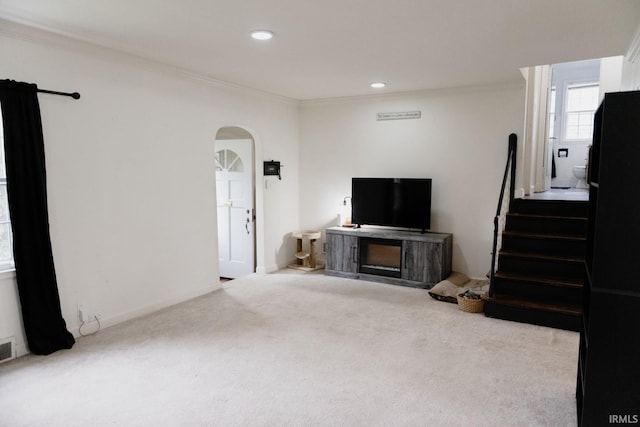 unfurnished living room featuring visible vents, arched walkways, ornamental molding, carpet, and stairs