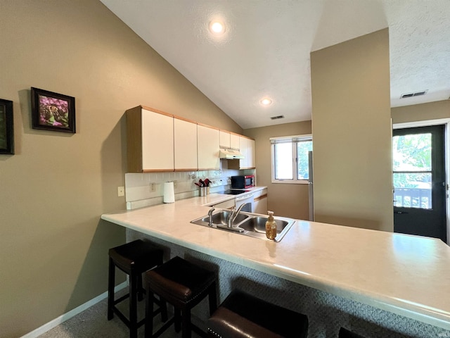 kitchen with a sink, light countertops, baseboards, a kitchen bar, and under cabinet range hood