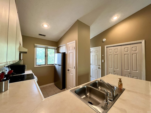 kitchen with a sink, visible vents, freestanding refrigerator, range hood, and vaulted ceiling