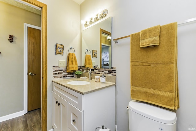 half bath with vanity, backsplash, toilet, and wood finished floors