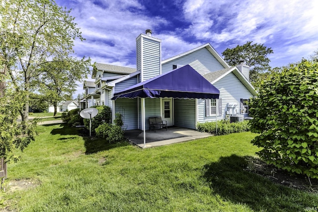 back of house featuring a patio, a chimney, a yard, and central AC