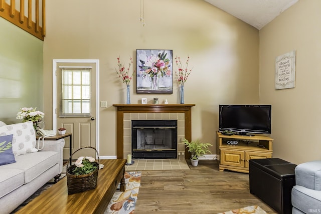 living area with a tiled fireplace, baseboards, wood finished floors, and high vaulted ceiling