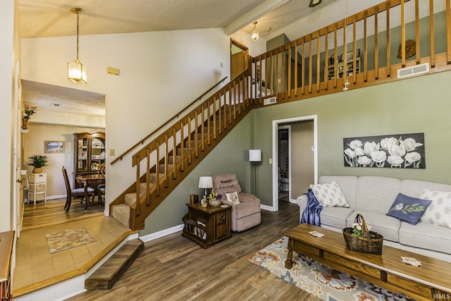 living room featuring visible vents, wood finished floors, stairway, high vaulted ceiling, and baseboards