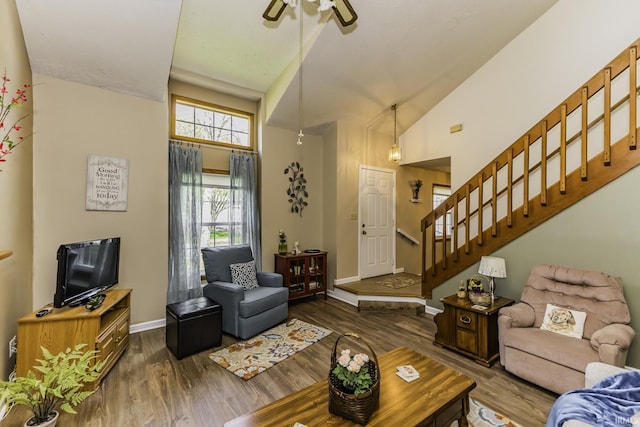 living area with high vaulted ceiling, stairs, a ceiling fan, baseboards, and wood finished floors