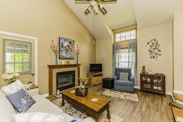 living area with high vaulted ceiling, a ceiling fan, baseboards, wood finished floors, and a tile fireplace