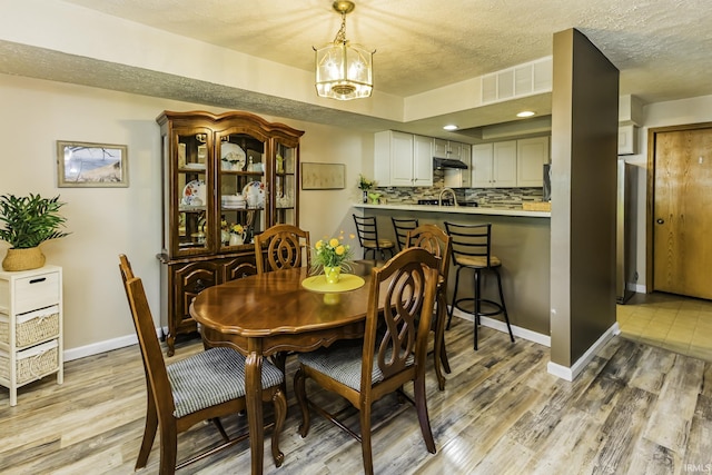dining area featuring visible vents, a textured ceiling, light wood-style floors, and baseboards