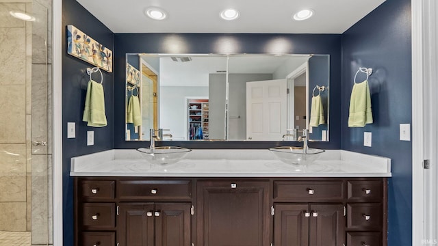 full bathroom featuring double vanity, a sink, a tile shower, and a spacious closet