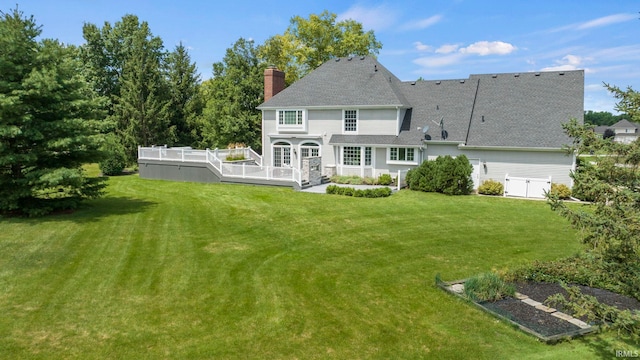 back of house with a garden, a wooden deck, roof with shingles, a chimney, and a yard
