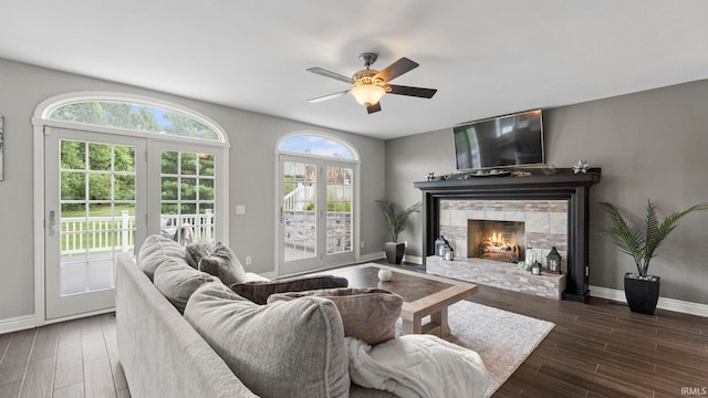 living room featuring a ceiling fan, baseboards, a stone fireplace, and wood finished floors