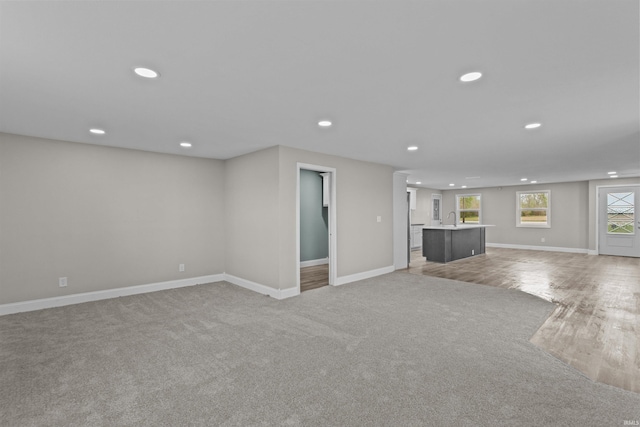 unfurnished living room with recessed lighting, baseboards, light colored carpet, and a sink