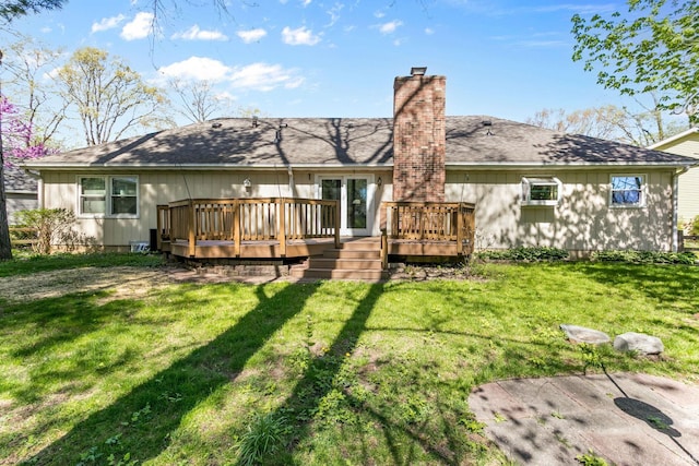 rear view of property featuring a lawn, a chimney, a shingled roof, and a wooden deck