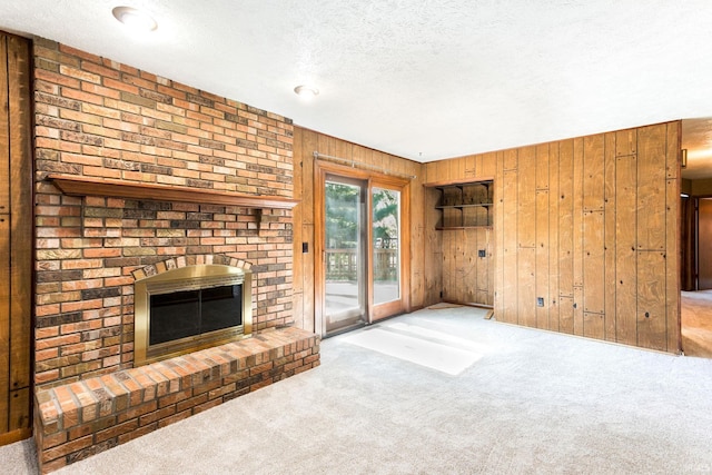 unfurnished living room featuring carpet flooring, a textured ceiling, wood walls, and a fireplace