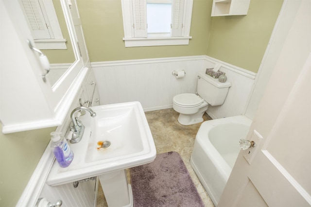 full bathroom with toilet, a tub to relax in, and a wainscoted wall