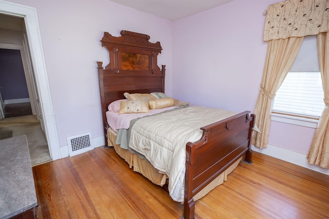 bedroom featuring baseboards, wood finished floors, and visible vents
