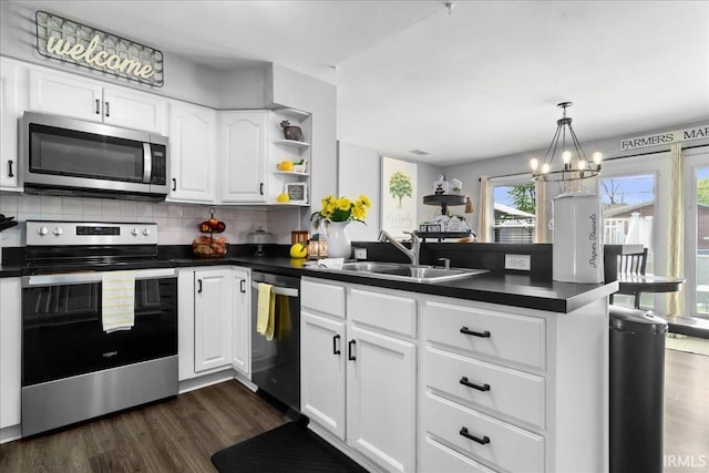 kitchen featuring a peninsula, dark countertops, a sink, a wealth of natural light, and stainless steel appliances