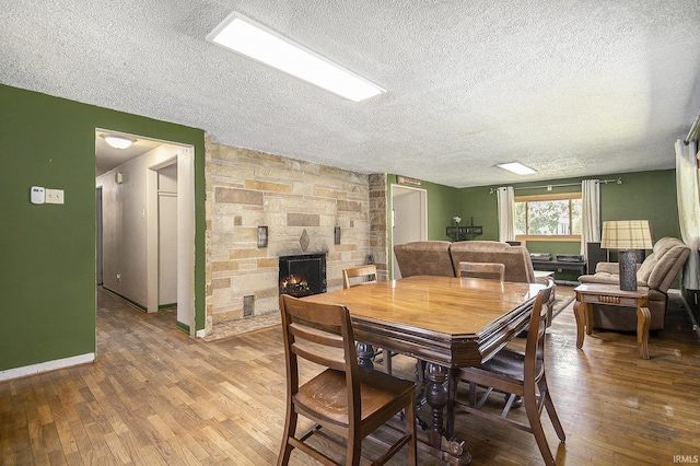 dining area featuring wood-type flooring, a textured ceiling, baseboards, and a fireplace