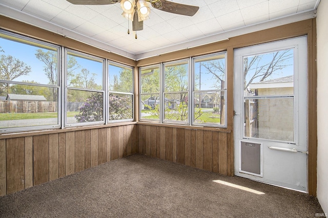 unfurnished sunroom with carpet floors, wood walls, and a wealth of natural light