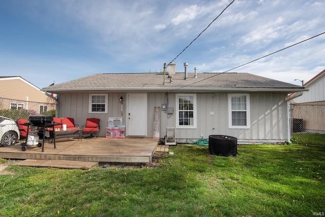 back of house featuring fence, a shingled roof, board and batten siding, a deck, and a yard
