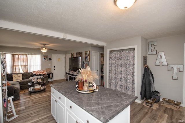kitchen featuring wood finished floors, open floor plan, a textured ceiling, white cabinets, and a ceiling fan