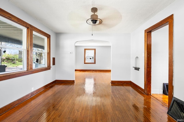 unfurnished room with arched walkways, baseboards, dark wood finished floors, and a ceiling fan