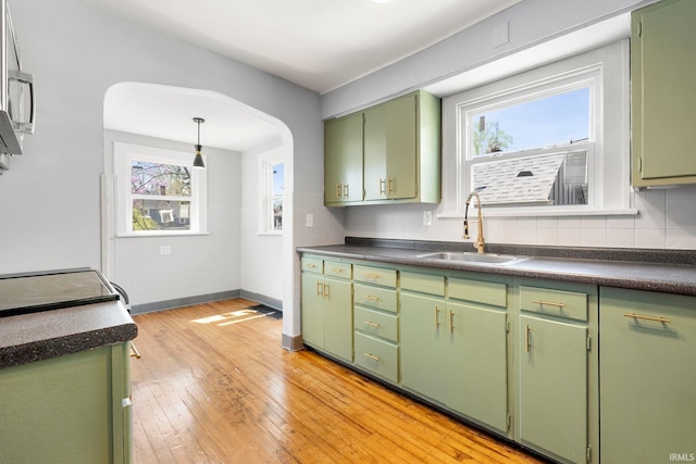 kitchen with dark countertops, tasteful backsplash, a sink, light wood finished floors, and green cabinetry