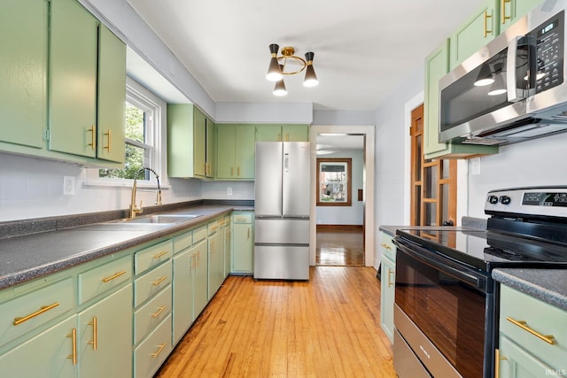 kitchen featuring backsplash, a sink, green cabinets, light wood finished floors, and stainless steel appliances