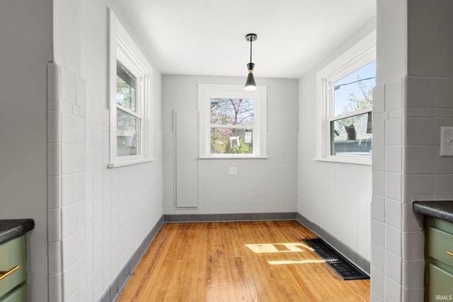 unfurnished dining area featuring tile walls, visible vents, a healthy amount of sunlight, and light wood-style flooring