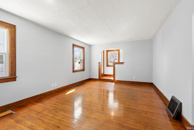unfurnished room featuring arched walkways, baseboards, a textured ceiling, and wood finished floors