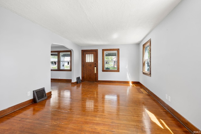 entryway featuring plenty of natural light, arched walkways, wood finished floors, and visible vents