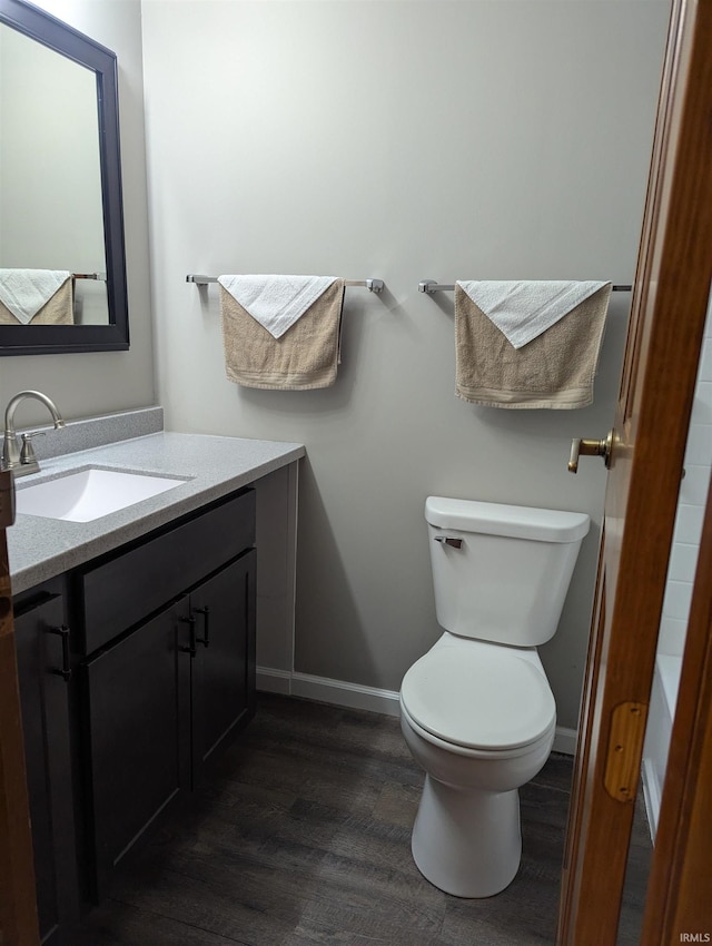 bathroom featuring toilet, baseboards, wood finished floors, and vanity