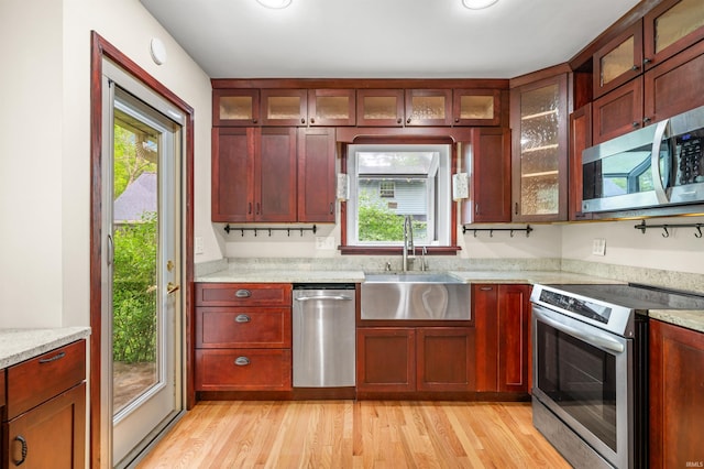 kitchen with appliances with stainless steel finishes, dark brown cabinets, a sink, light stone counters, and light wood-style floors