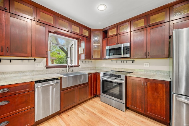 kitchen featuring a sink, appliances with stainless steel finishes, light wood finished floors, and light stone counters